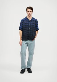 Mørkeblå kortermet skjorte med rutemønster, parret med lyseblå bukser og svarte sko. Glatt stoff, avslappet passform, knappelukking.