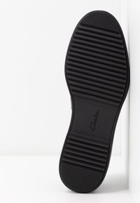 Semelle de chaussure en caoutchouc noir avec des rainures horizontales et une section lisse. Marque "Clarks" embossée sur le bord extérieur.