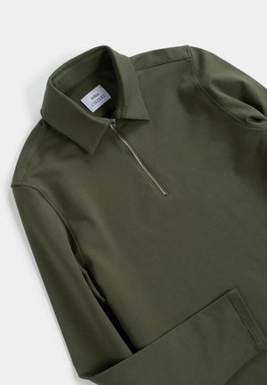 Maglione verde oliva con colletto a zip, caratterizzato da maniche lunghe e un tessuto liscio e leggermente strutturato. Etichetta del marchio visibile all'interno del colletto.