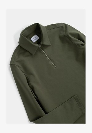 Maglione verde oliva con colletto a zip, caratterizzato da maniche lunghe e un tessuto liscio e leggermente strutturato. Etichetta del marchio visibile all'interno del colletto.