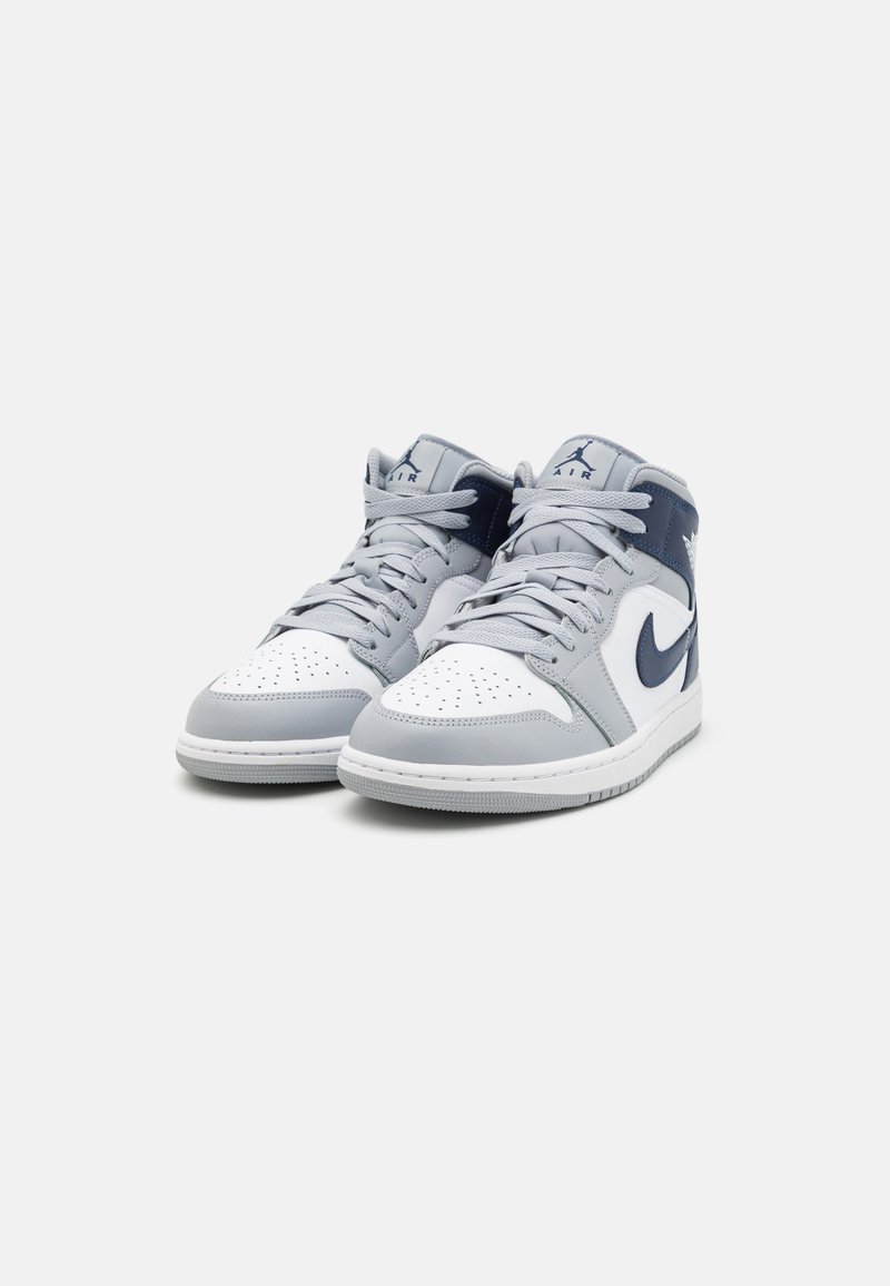 Zapatillas altas de cuero gris claro y blanco, con un swoosh azul marino, punta redonda y secciones perforadas para mayor transpirabilidad.