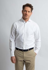 Witte button-up shirt met een gestructureerde kraag, lange mouwen en subtiele textuur, gecombineerd met khaki broeken en een zwarte riem.