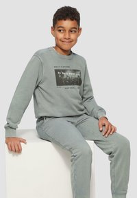 Sudadera de algodón gris y pantalones a juego. La sudadera presenta un estampado gráfico con texto. Textura suave y ajuste relajado en todo.
