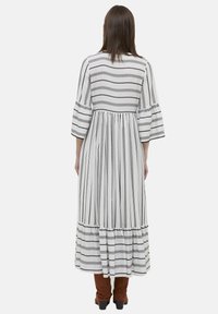 Dlouhé pruhované šaty bílé a černé barvy s volnými rukávy, vrstveným designem a vzdušnou siluetou. Tkanina vypadá lehce a texturovaně.