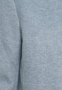 Hellblauer Stoff mit einem strukturierten Strickmuster, der eine weiche und leicht flauschige Oberfläche aufweist. Das Material scheint dehnbar und atmungsaktiv zu sein.