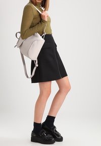 Gonna nera con zip frontale e tasche, top lungo olive a maniche lunghe, borsa a tracolla in pelle grigia e scarpe platform nere con dettagli in pelliccia.