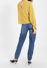 Haut à manches longues rayé jaune avec découpe dans le dos, associé à un jean en denim bleu taille haute et des escarpins noirs à bout pointu.