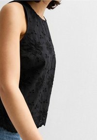 Top sin mangas negro con bordado floral, que presenta una tela texturizada, un escote redondo y un dobladillo en forma de ola. Combinado con denim.