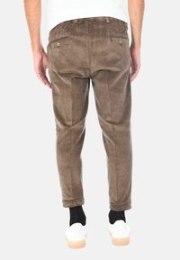 Pantaloni di corduroy marroni con strisce verticali, dotati di due tasche posteriori e orli a risvolto, indossati con sneaker bianche e calzini neri.