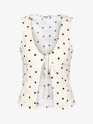 Blouse blanche sans manches à pois noirs, col en V profond, avec fermeture nouée à l'avant.