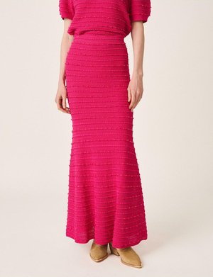 Mujer con una falda larga y texturizada de punto rosa fuerte combinada con un top a juego y botines color topo con punta afilada.