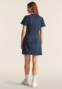 Vestido navy de manga corta con un diseño simple, corte recto y costura en la parte trasera. Llevado con calcetines blancos y zapatillas blancas.