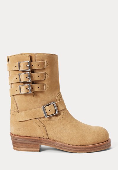 Rjavi semiš gležnjar z okroglim prstom, tremi srebrnimi zaponkami in gomilnim lesenim peto. Gladek teksturni videz z minimalnimi šivi.