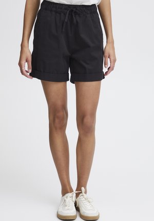 Pantaloni corti neri in cotone con orlo arrotolato, cinturino elastico e dettaglio con cordino, abbinati a sneakers bianche su uno sfondo neutro.