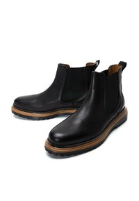 Botas Chelsea de cuero negro con paneles elásticos laterales, superficie texturada y suela de goma marrón. Cuentan con tiradores para facilitar su uso.