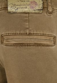 Ruskea kangas, jossa on sileä pinta, sisältää ommellun takataskun ja vyötäröllä olevan haalistuneen painatuksen.