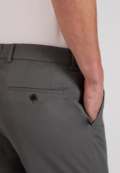 Gros plan d'une personne portant un pantalon gris foncé avec une poche arrière boutonnée et la main placée dans la poche latérale avant.