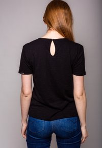 Black short-sleeve t-shirt featuring a back keyhole design and a textured fabric. Paired with fitted blue denim jeans.