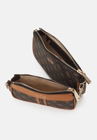 Dvě zipové kosmetické tašky v hnědé a béžové monogramované tkanině, s zlatým kováním a hladkým povrchem, naskládané na sobě pro vystavení.