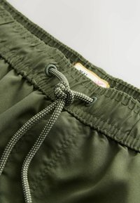 Rohelised kergelt siledast kangast paelaga lühikesed püksid, millel on metallist silmused ja vöökoha ümber sõlmitud pael.