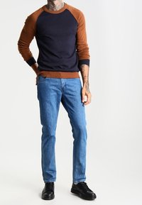 Camisa de manga larga en náutico y marrón con mangas raglán, combinada con jeans de color azul claro y zapatos de cordones negros. Presenta un cuello y puños acanalados.