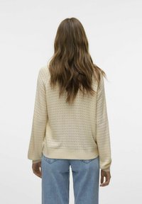 Maglione lavorato a maglia color crema con un motivo testurizzato, maniche lunghe e polsini a coste. Abbinato a jeans azzurri chiari, leggermente affusolati.
