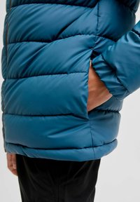 Padded jacket v tehlové barvě, s prošívaným designem, postranní kapsou s kontrastní hnědou tkaninou a volným střihem. Hladký, lesklý povrch.