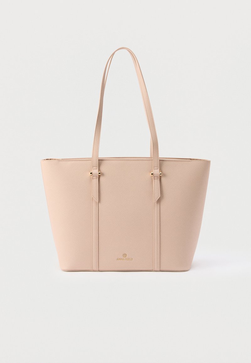 Sac cabas en cuir beige avec double anse d'épaule et logo doré subtil sur le devant, posé sur un fond clair uni.