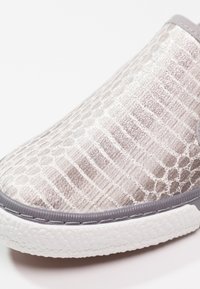 Gros plan sur une chaussure argentée à enfiler texturée avec un motif hexagonal en relief et une semelle blanche rainurée.