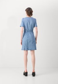 Denimkleit lühikeste varrukatega, vöödiga talje, A-line siluett, helesinine värv ja kontrastsetest õmblustest detailid. Lamedad kingad.