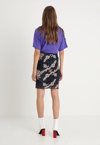 Fialové oversized tričko, černá sukně s abstraktním béžovým a námořnickým vzorem a bílé kotníkové boty s červenými blokovými podpatky.