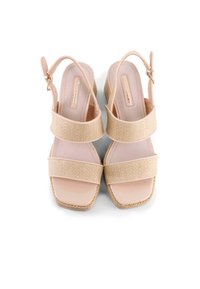 Las sandalias de cuña beige presentan una zona de toe en cuero charol suave, dos correas trenzadas y un talón con una hebilla ajustable.