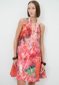 Une robe sans manches aux motifs floraux vibrants rouges et roses, fabriquée à partir d'un tissu léger, avec un décolleté en V et une silhouette évasée fluide.