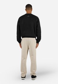 Black, plush knit sweater with ribbed cuffs and hem, paired with beige, relaxed-fit trousers, completed with black sneakers.