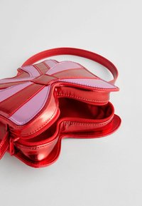 Červená a ružová metalická crossbody taška v tvare motýľa, ktorá má dva zipsové oddelenia a hladký povrch na vonkajšej strane.