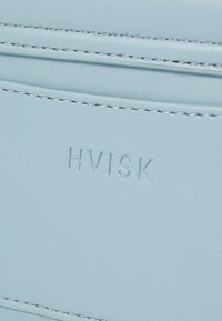 Lys blå lærplånbok med preget 'HVISK'-logo, med sømdetaljer og glatt tekstur, som fremhever et minimalistisk design.