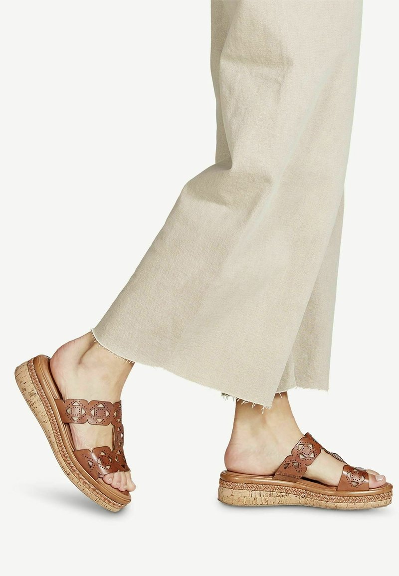Sandales en cuir marron avec des découpes florales et une semelle en liège. Dessus texturé et détails de la sangle visibles.