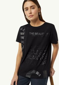 Schwarzes T-Shirt mit kurzen Ärmeln aus Baumwolle, versehen mit verschiedenen strukturierten Grafikdrucken in metallic Silber, die Phrasen und kreisförmige Designs zeigen.