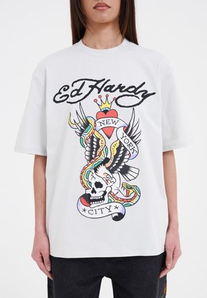 White cotton t-shirt featuring a large colorful graphic print of a skull, eagle, snakes, and text saying "Ed Hardy New York City."