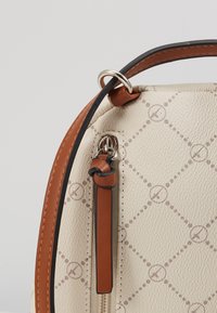 Sac en cuir à texture crème avec garniture marron clair, anneau en métal et tirette de fermeture éclair ornée d'un détail de lanière en cuir marron clair nouée.