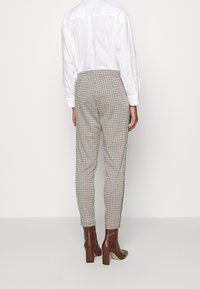 Pantalon à carreaux en teintes claires avec une coupe slim, présentant une texture lisse et associé à des bottines marron. Vue arrière visible.