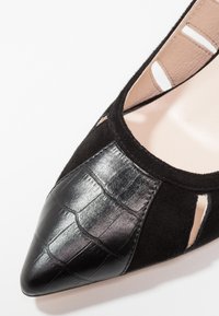 Chaussure plate noire à bout pointu avec embout en cuir embossé crocodile et détails découpés en daim sur les côtés.