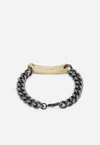 Pulseira de corrente em metal negro com uma etiqueta retangular em tom dourado com texto gravado, fixada com um fecho redondo.