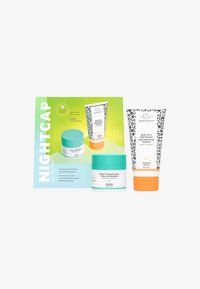 Nightcap skincare set featuring a teal jar, a white jar with orange accents, and a patterned cleanser tube, all on a green background.