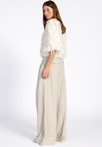 Witte getextuurde cropjack met gelaagde accenten, gecombineerd met lichtbeige high-waisted broek met wijde pijpen die licht gekreukt zijn.