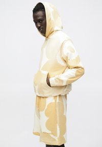 Sweatshirt com capuz e calções em amarelo claro com padrões florais brancos, feitos de tecido macio, com bolso frontal e cintura com cordão.