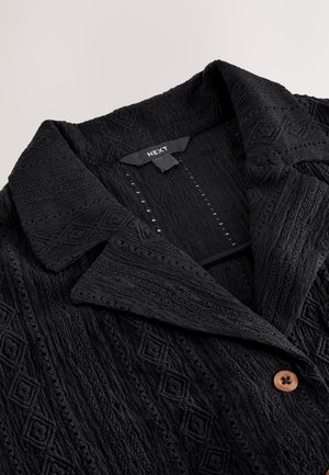 Giacca nera testurizzata con motivo a diamante, colletto a incavo e chiusura con bottone in legno, etichettata "NEXT". Tessuto morbido e tessuto.