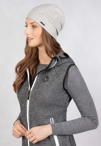 Jasnoszara dzianinowa czapka z prążkowanym wzorem. Nosi się ją z ciemnoszarym kamizelką z zapięciem na zamek i akcentem logo.