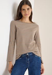 Gestreiftes Langarmoberteil aus weichem Beige- und Weißstoff mit weitem Ausschnitt. Kombiniert mit dunkelblauen Jeans, die ein dezentes Eingrifftaschendetail aufweisen.