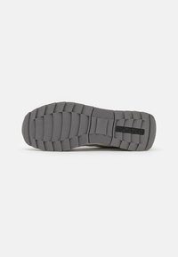 La suola delle sneaker grigia presenta un design in gomma testurizzata con profonde scanalature e una superficie a motivi per la trazione. Logo visibile al centro.